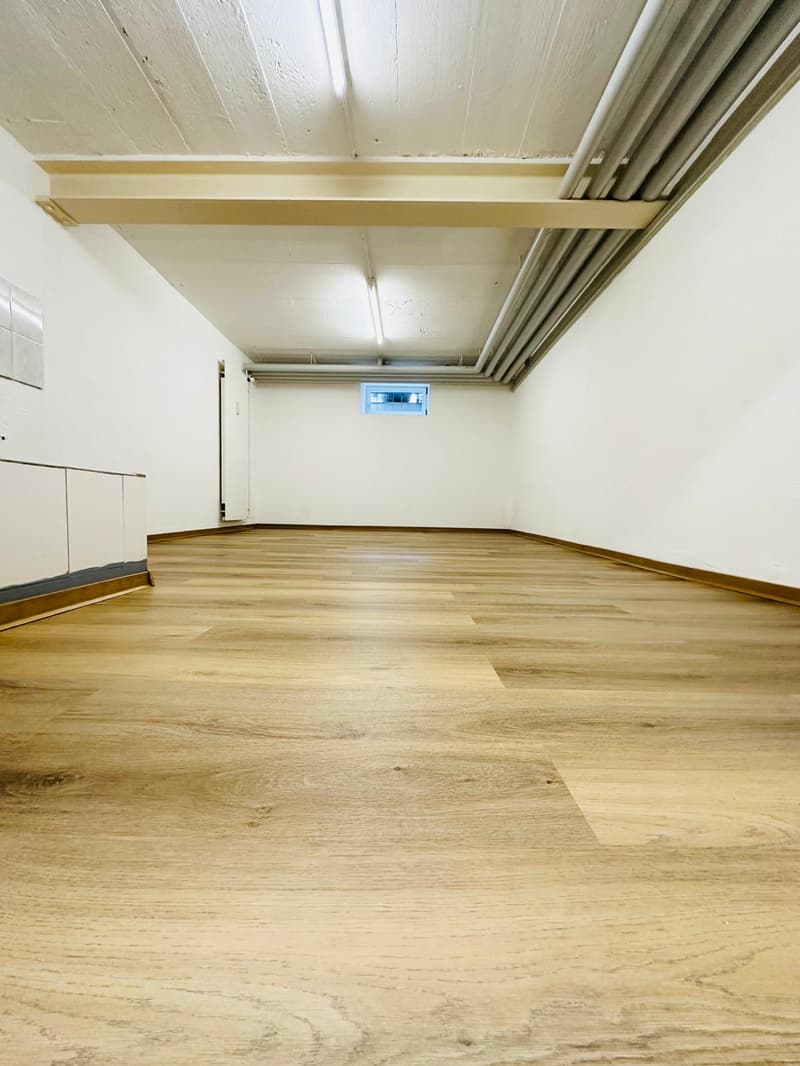 Empty room, hardwood floors, white walls, ceiling with visible beams, small window on the wall, white cabinets along the wall.