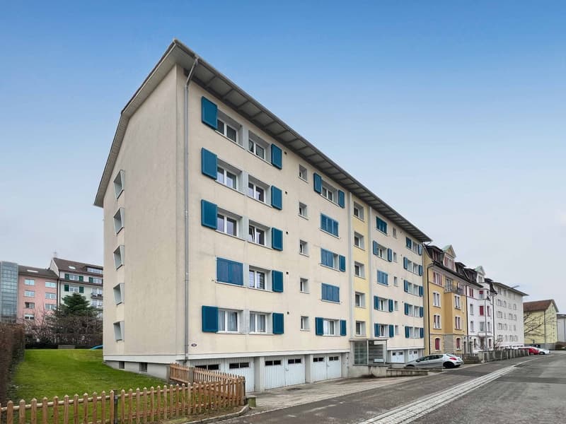 5 story building, white walls, blue shutters, 3 garages at the bottom