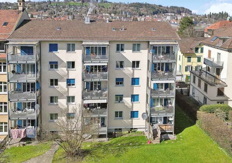 4 story apartment building with multiple balconies, tiled roof, and some windows have blue shutters