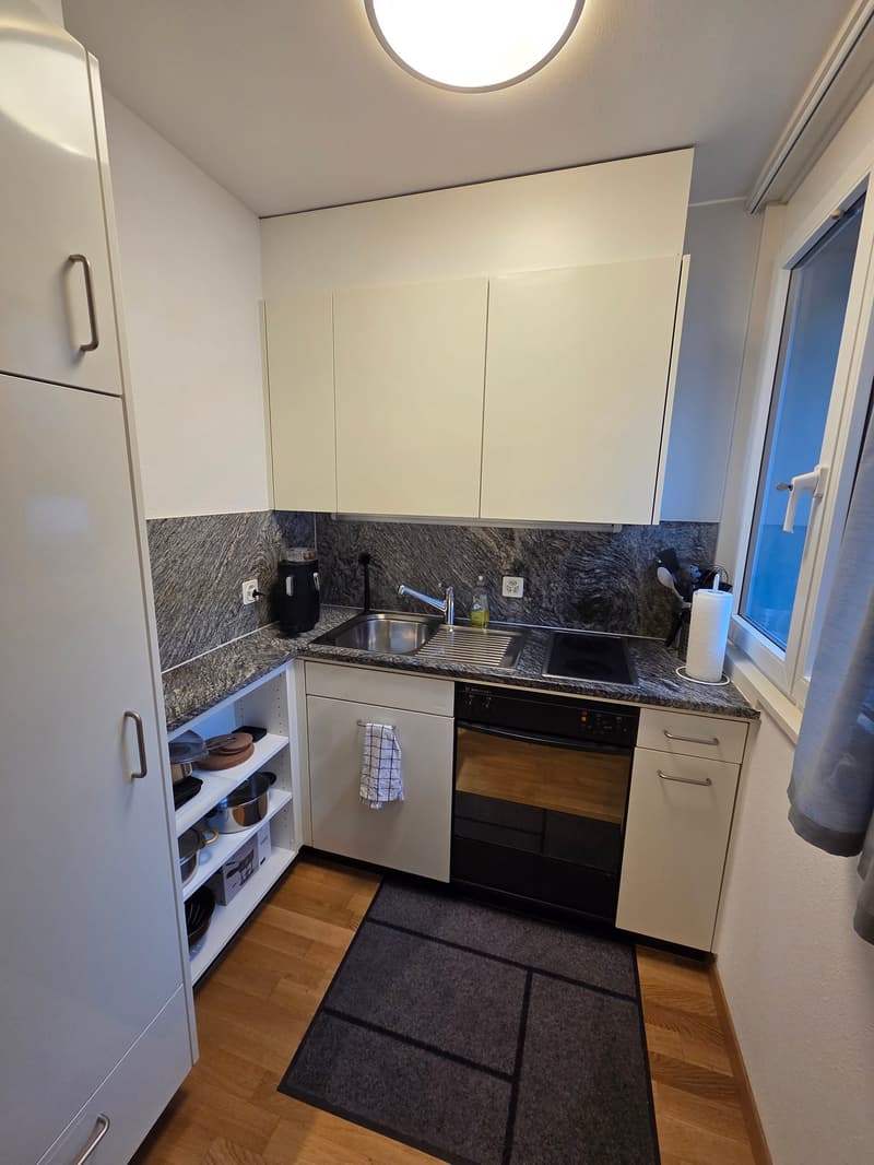 Modern and well-equipped kitchen with granite countertops, stainless steel sink, dishwasher, washing machine, built-in cabinets, and a window.