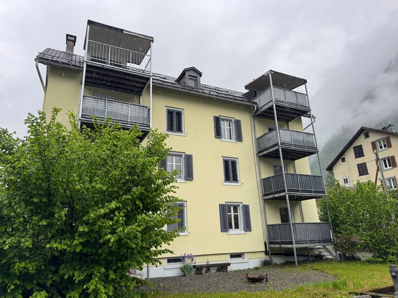 yellow building, balconies, multiple floors, white windows, trees, gravel