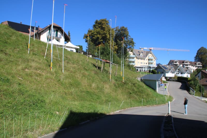 Houses on a sloped area with a large grassy hill, road, construction crane, and people in the background
