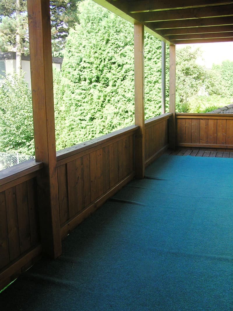 wooden railings, wooden floor, green carpet, view of trees
