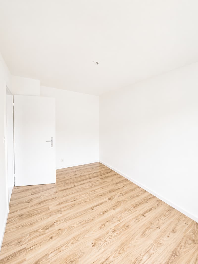 Empty room with white walls, wooden floor, white door, power outlet on the wall