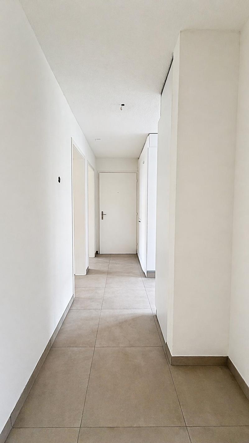 Empty hallway, white walls, tiled floor, two doors, one with a handle