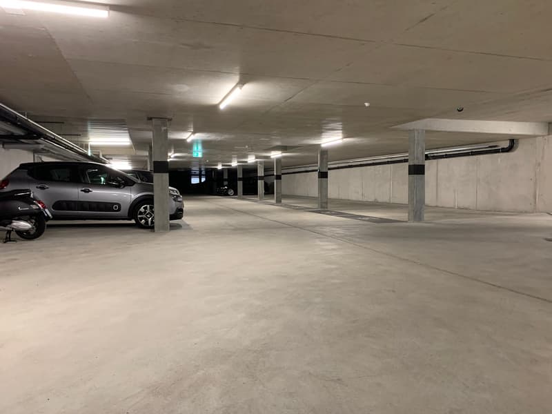 underground parking lot, concrete floor, metal pillars, ceiling lights, parked car, motorcycle