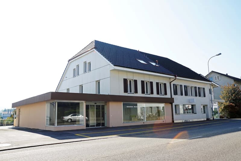 2-story commercial building with white exterior, blue roof, large windows, and a parking area in front