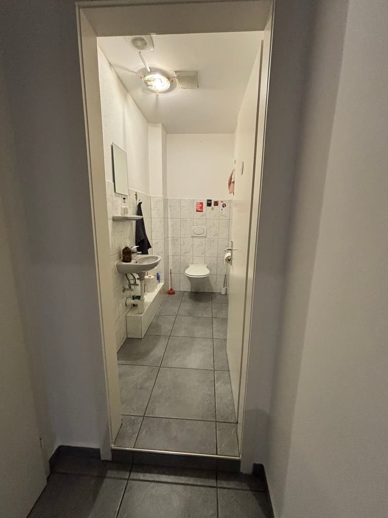 Tiled floor, white walls, sink, toilet, mirror, lighting fixture