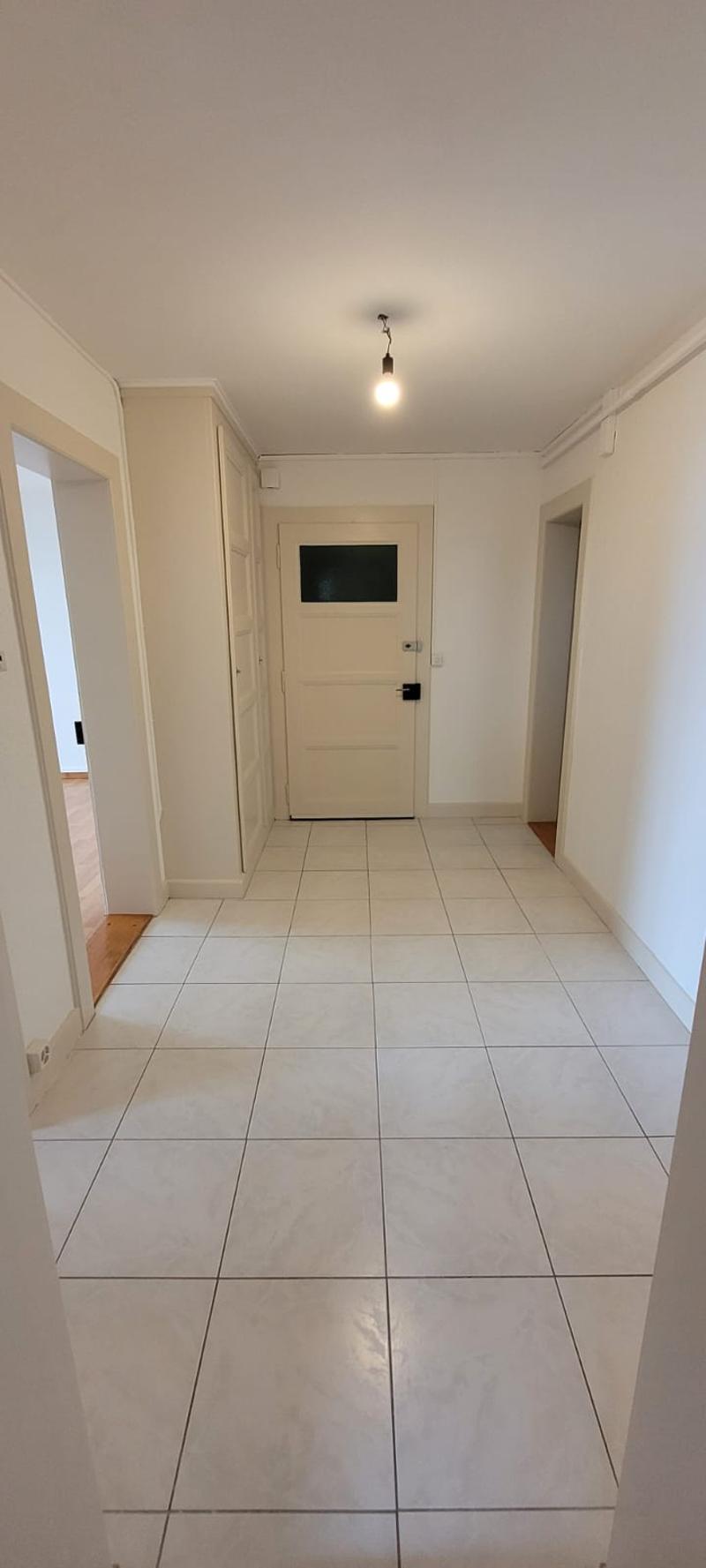 a hallway with white tiles, white walls, two doors, and a lamp