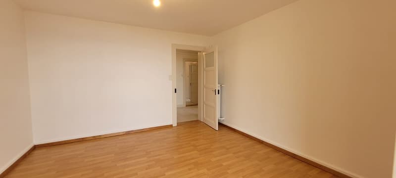 wooden floor, white walls, open door to another room, white tile in the corridor