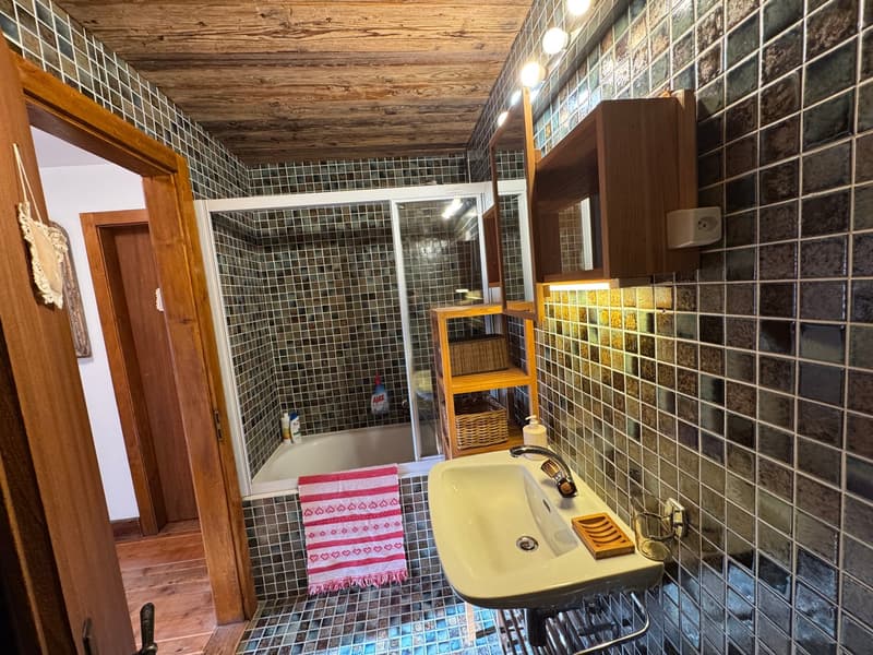 Bathroom with wooden ceiling, tiled walls, bathtub, sink, mirror, wooden shelves, towel hanging on the wall, wooden floor