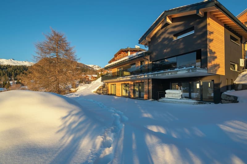 modern chalet, wooden exterior, large windows, balcony, surrounded by snow