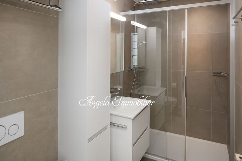 white vanity, glass shower enclosure, wall-mounted showerhead, white walls, beige tiles, toilet, bidet, hanging towel rack