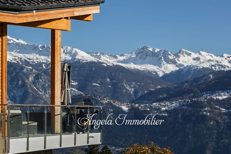 Wooden chalet-style building with a balcony overlooking a snowy mountain landscape. The building has the name 'Angela Immobilier' displayed on the front.