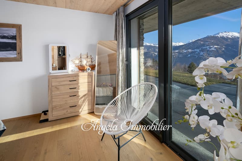 Spacious bedroom with large windows offering a scenic mountain view, wooden dresser, and a comfortable chair overlooking the outdoor terrace