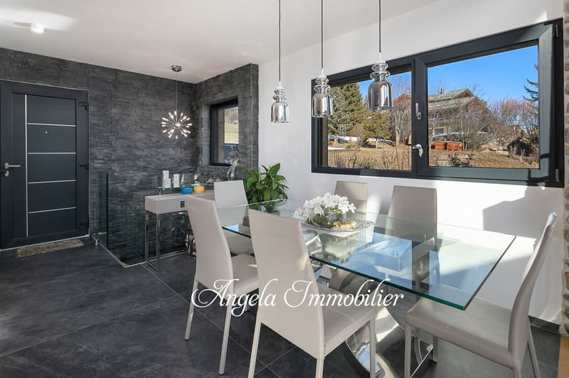 Modern dining room with glass dining table, white chairs, pendant lights, and large windows overlooking a scenic outdoor view.