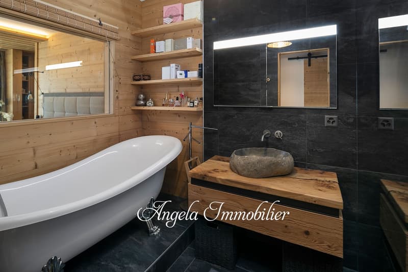 Spacious bathroom with wooden walls, large bathtub, vanity with stone sink, and shelves for storage