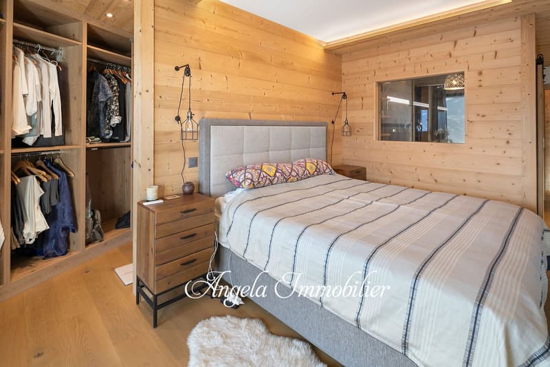 Spacious bedroom with wooden walls and ceiling, large bed with gray upholstered headboard, nightstands, closet space, and pendant lighting fixtures