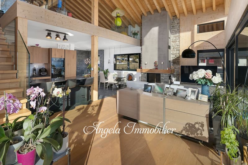 Spacious open-plan office with wooden beamed ceiling, stone walls, modern furniture, and a fireplace. The space includes a reception desk, seating area, and kitchen appliances. Decorative plants and flowers add a touch of nature to the interior.