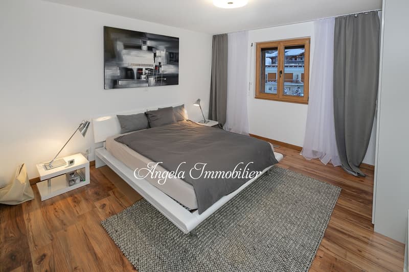 Spacious bedroom with hardwood floors, large windows, modern abstract artwork, and a cozy bed with gray bedding