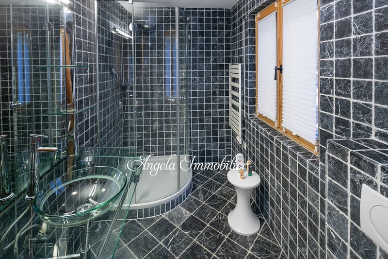 modern bathroom with glass shower, black marble tiles, glass sink, white toilet, glass shelves, white window blinds