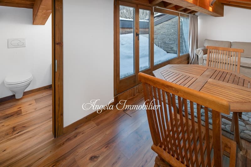 wooden floor, white walls, large windows, wooden table and chairs, toilet, rug, couch
