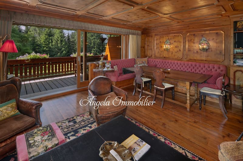 Wooden walls and floor, balcony, couch, dining table with chairs, window with glass door, lamp, rug, picture frames