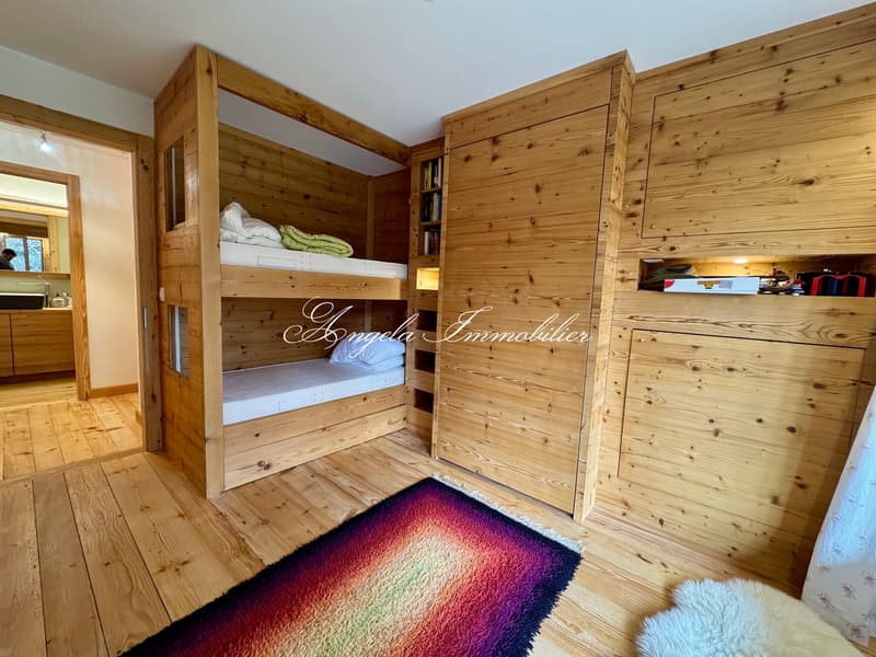 wooden bunk beds, books on shelves, rug on the floor, wooden walls and flooring