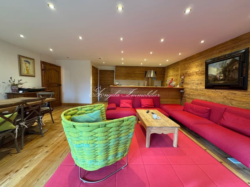 open layout with living area and dining table, wooden walls, coffee table, two large red sofas, green armchair