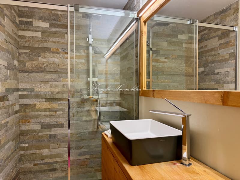 Shower stall, sink with wooden vanity, mirror, and stone wall tiles