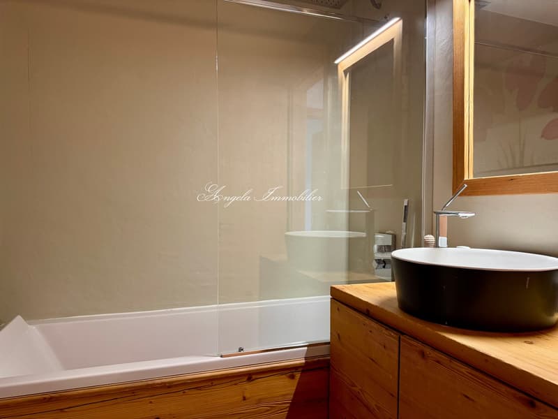 Modern bathroom with a bathtub, shower, vanity with sink, wooden cabinets, and glass shower enclosure.