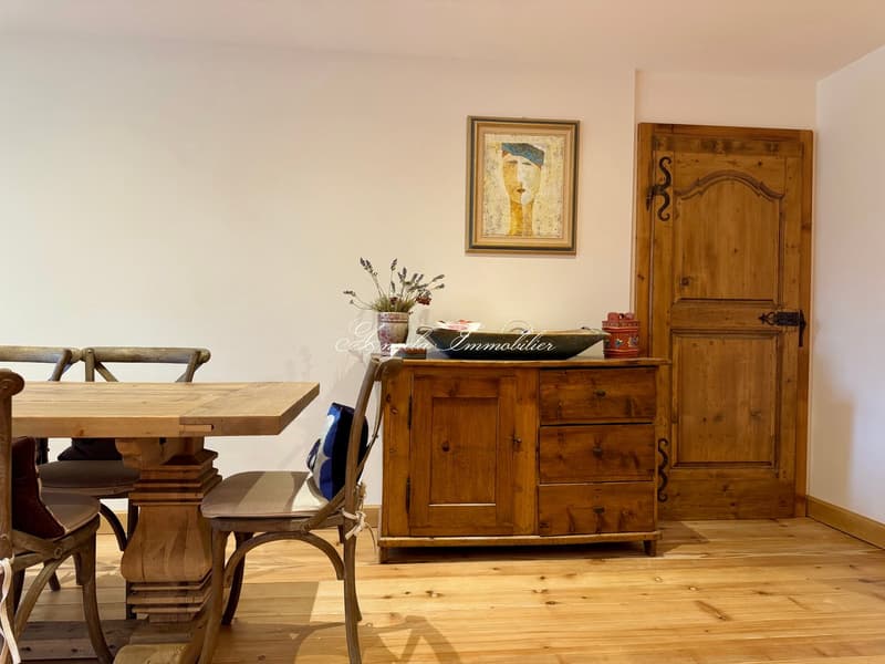 Dining room: wooden floor, dining table, wooden chairs, wooden cabinet, wooden door, painting, flowers