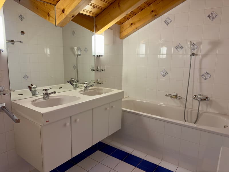 Bathroom with a white bathtub, white sink with two faucets, white cabinets, white tiled walls, and blue tiles at the base.