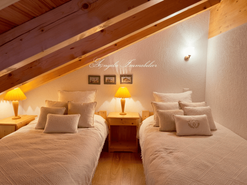 Bedroom with two beds, wooden nightstands, lamps, pillows, and wall-mounted pictures.
