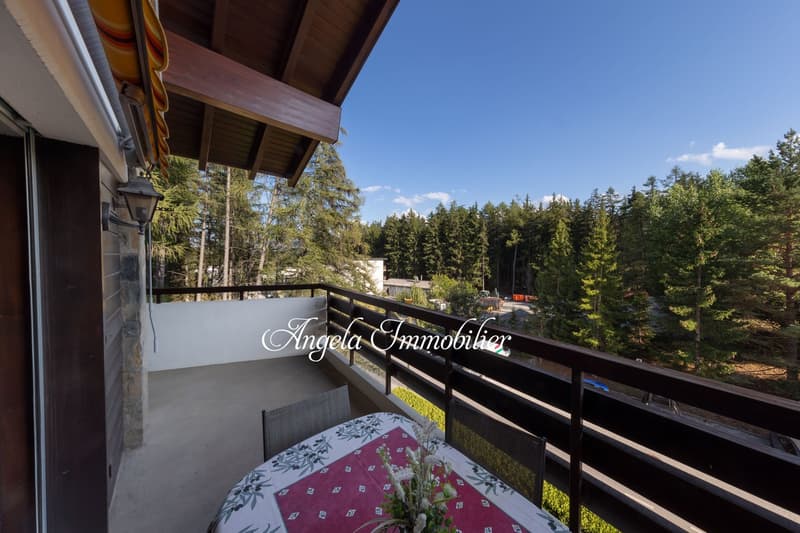 Outdoor balcony, table with flowers, wood railing, forest view, partial roof cover
