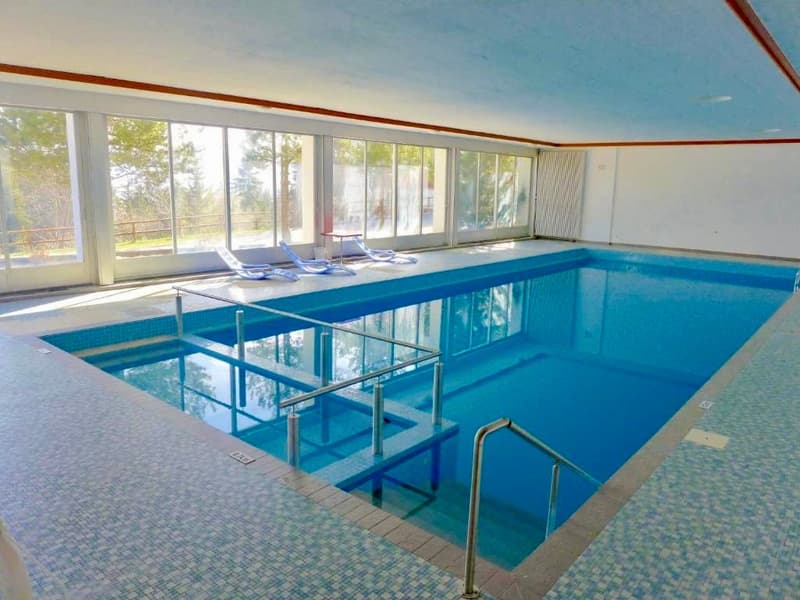 indoor pool, glass walls, large pool, deck chairs, tile flooring, scenic view