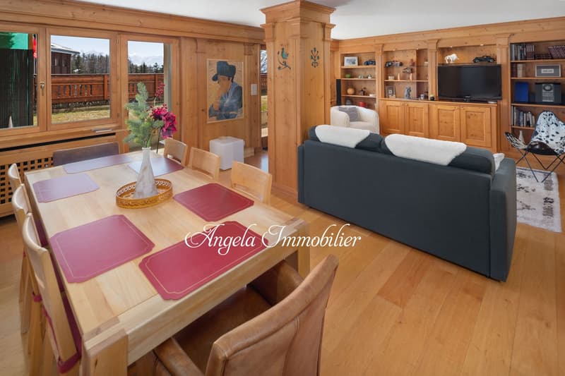 Dining area with wooden table and chairs, couch, television, bookshelves, wooden interior design