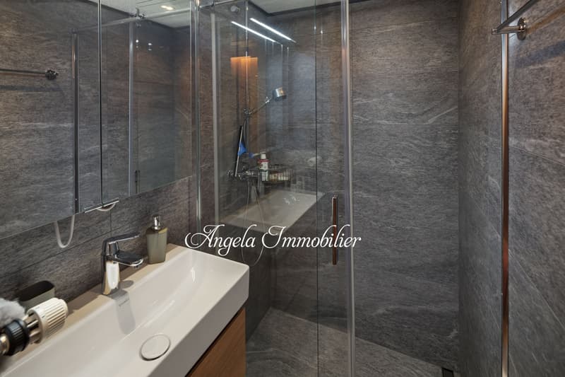 White sink, grey tiled walls, glass shower cubicle, wooden cabinet, shower head