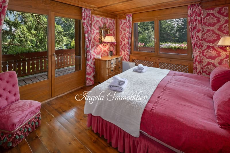 wooden floor, large bed, pink bedspread, wooden cabinet, lamp, balcony, window, view of trees
