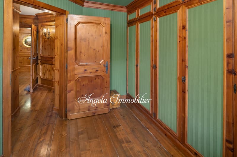 Rustic wooden interior with green walls, wooden paneling, and a large wooden cabinet or armoire. The room has a warm, cozy feel with wooden floors and a fireplace visible.