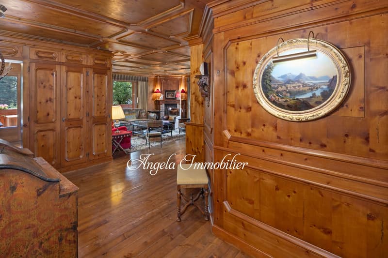 Spacious living room with wooden paneled walls and ceiling, hardwood floors, large ornate framed mirror, fireplace, and various furniture pieces including a sofa and chairs.