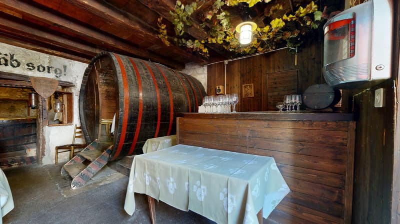 Dining area with wooden table, chairs, barrel, hanging lamps, shelf with framed picture, and wine glasses