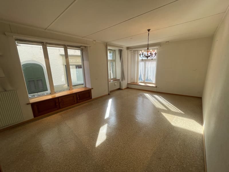 empty room with two large windows, wooden window seats, white radiators, wooden floor, central chandelier