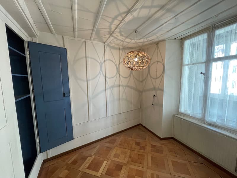 Empty room with wooden floor, blue door, hanging lamp, white walls, and large window