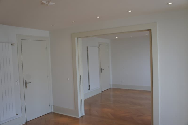 Empty room with white walls, wooden floor, two doors, and a radiator