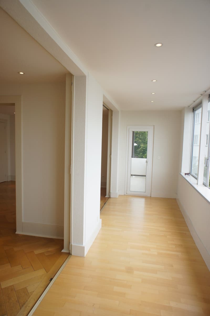 Empty room with wooden floor, white walls, balcony, windows