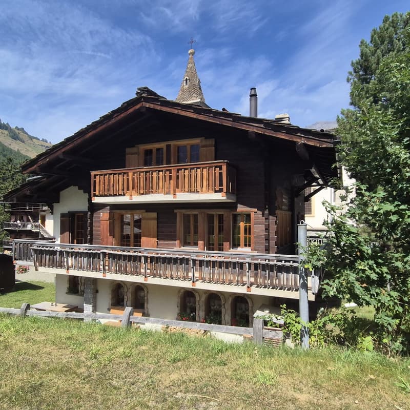 Wooden Swiss cottage, two stories, steep roof, balcony, terraced ground floor, view of the mountains