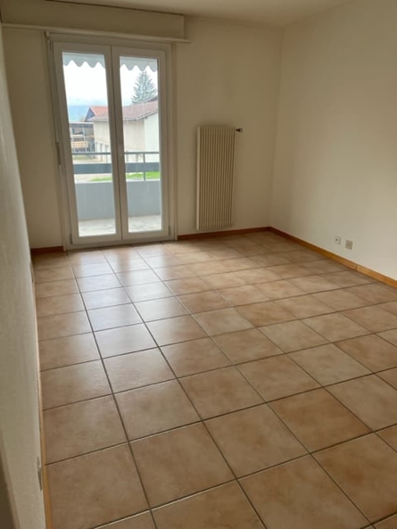 Empty room, large windows, balcony with railings, sliding glass doors, tiled floor, white walls, radiator
