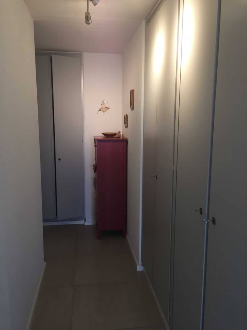Empty hallway with tiled floor, two white sliding doors, a red cabinet, and a ceiling light