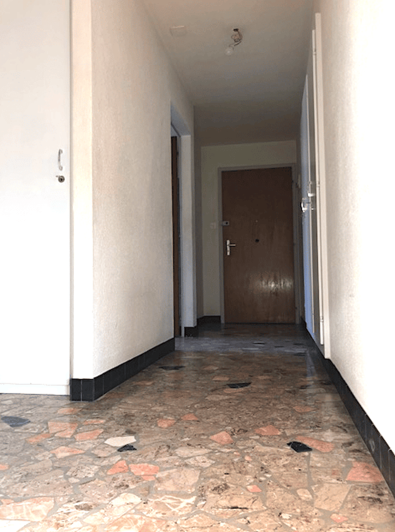 Empty hallway with white walls, brown door, stone floor